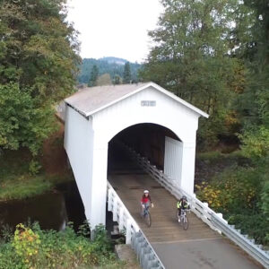 Cyclists ride through a covered bridge.