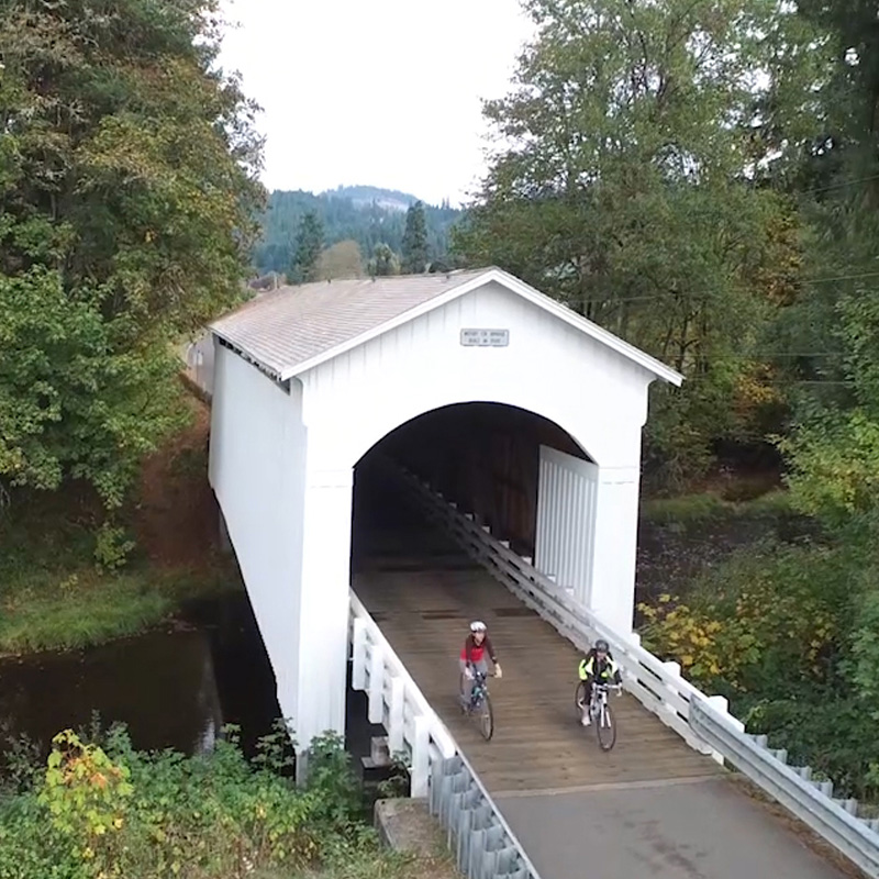 Cyclists ride through a covered bridge.