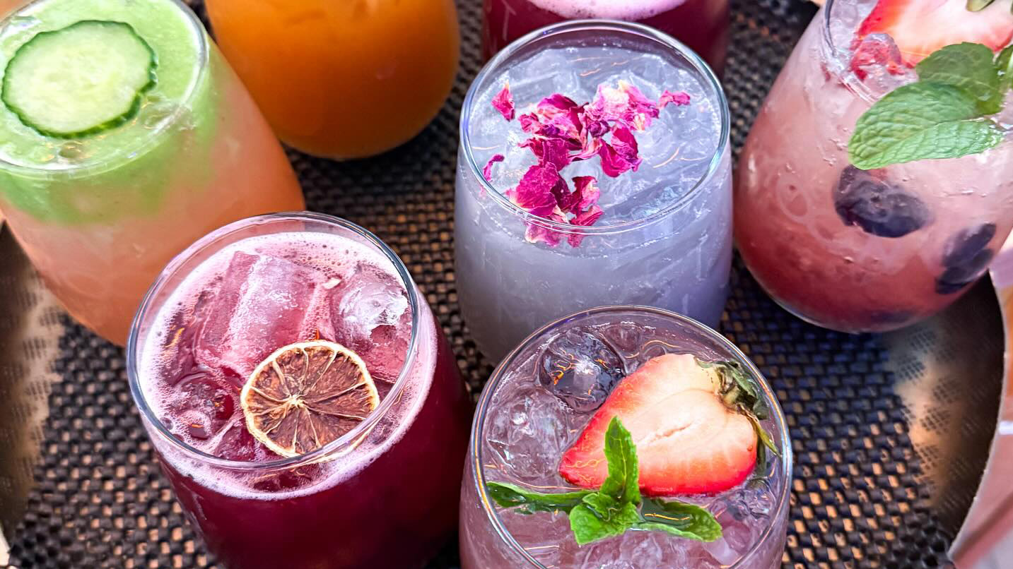 Colorful drinks with flower and fruit garnishes.