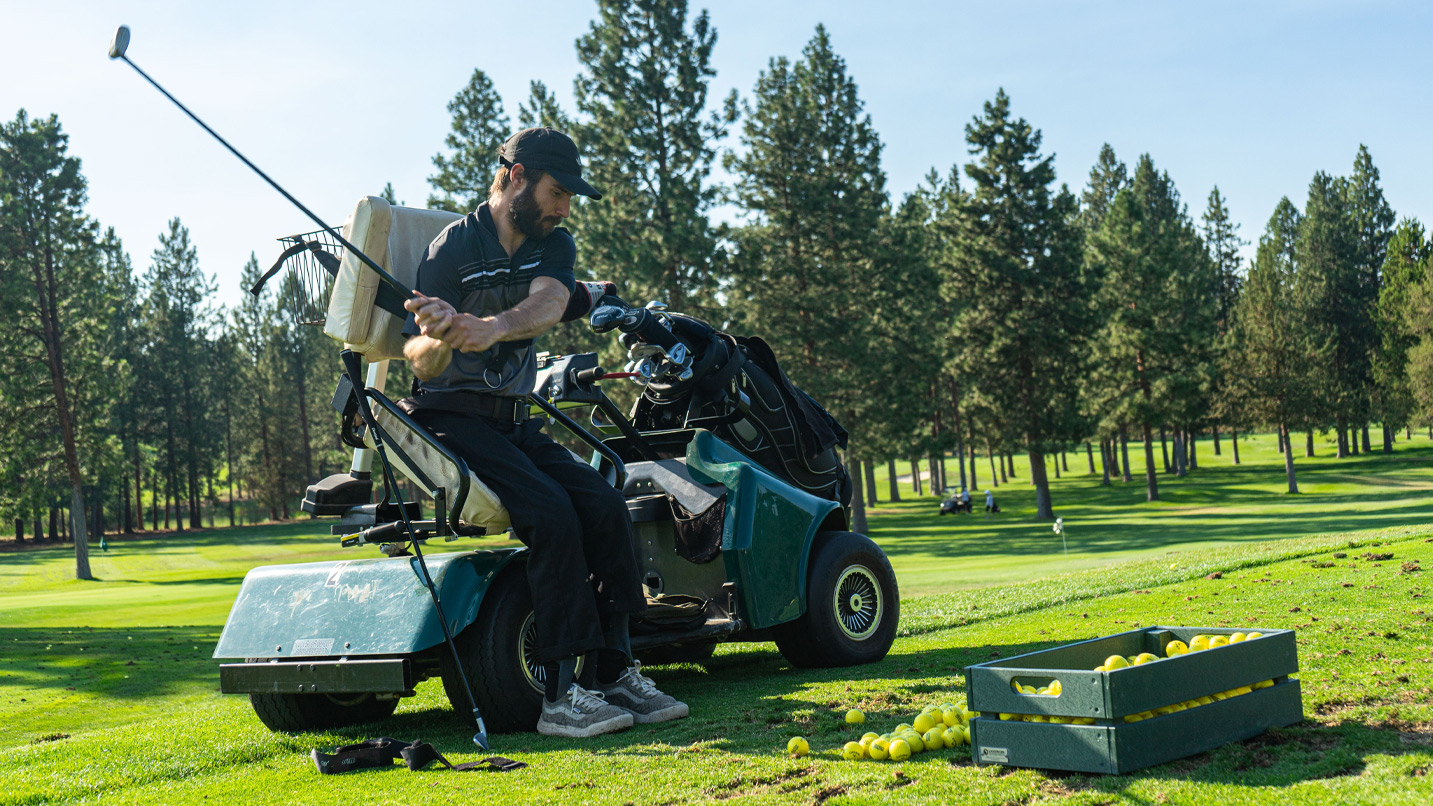 A man using an golf cart equipped with accessibility tools to stand for a golf swing.