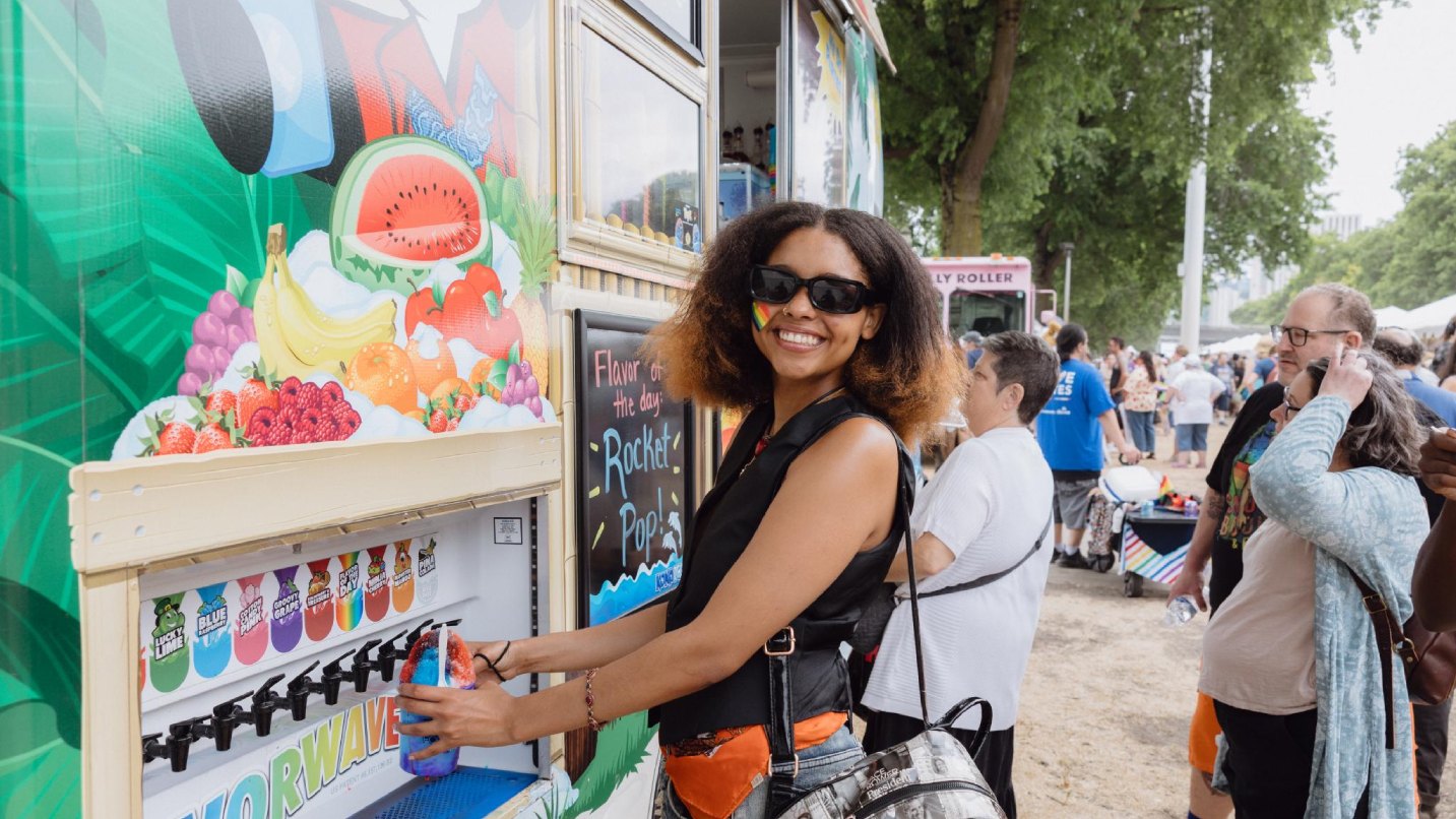 A young black woman smiles as she pours a slushie from a food truck's dispenser.