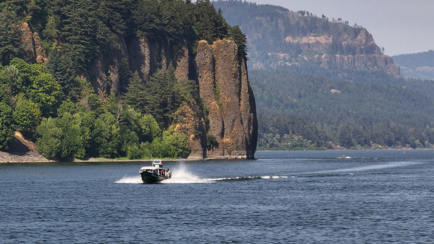 A jetboat speeds pass a towering cliff.