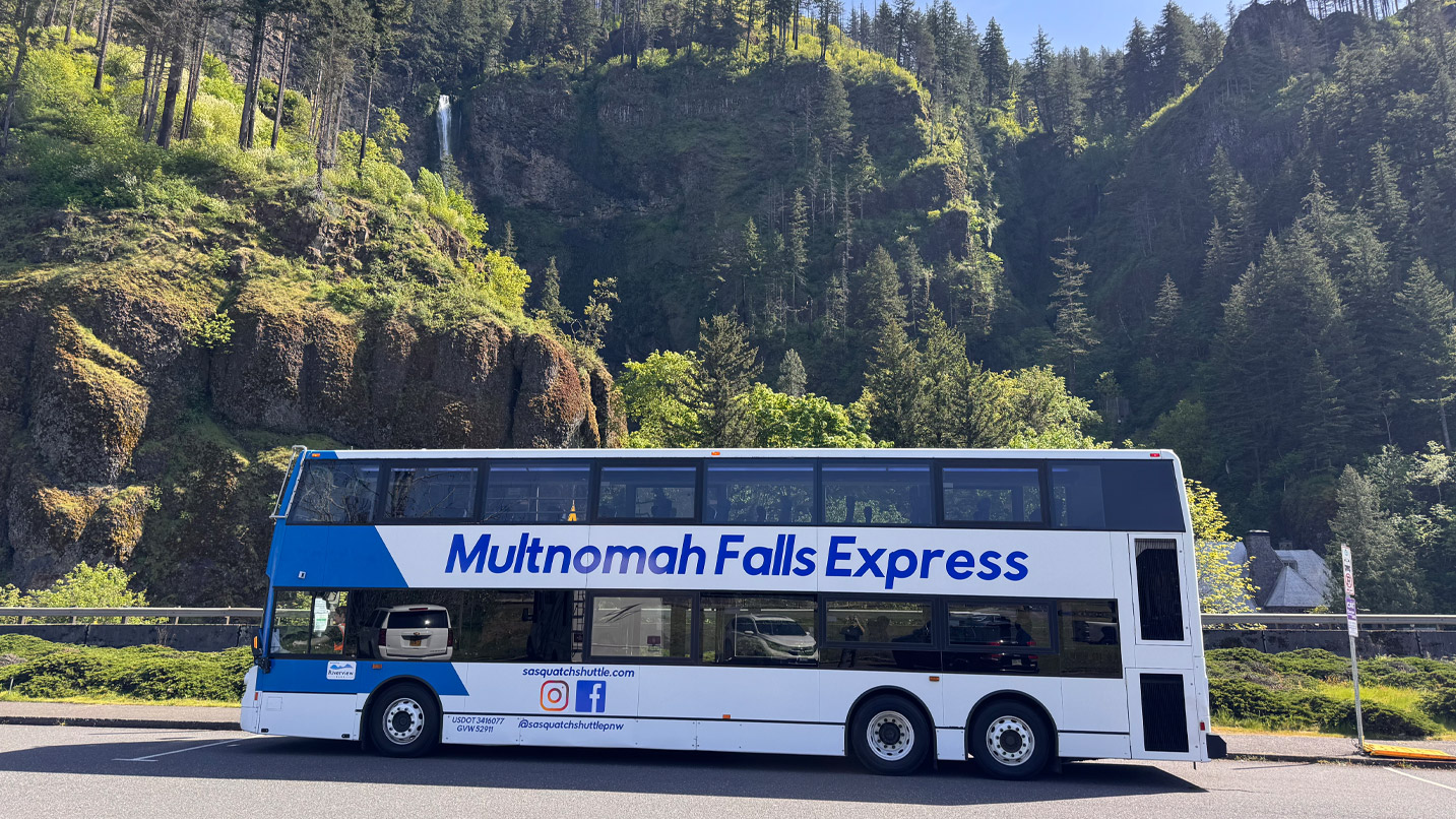A double-decker bus parked in front of a waterfall.