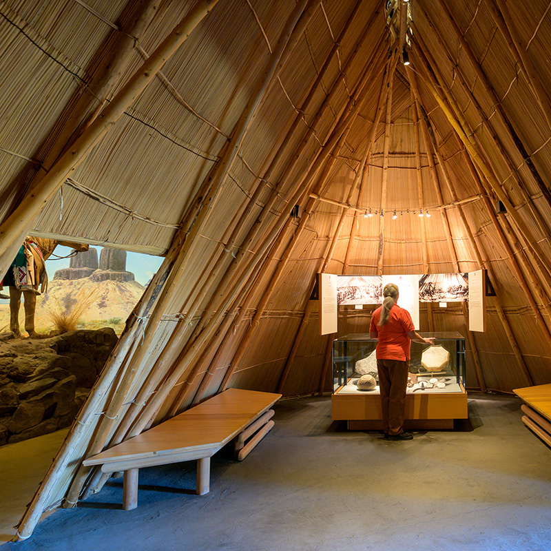 A woman stands in a recreated wooden teepee.