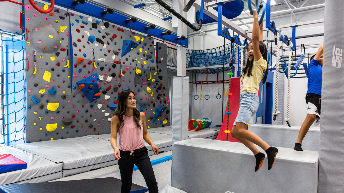 Kids swing across monkey bars in an inside gym.