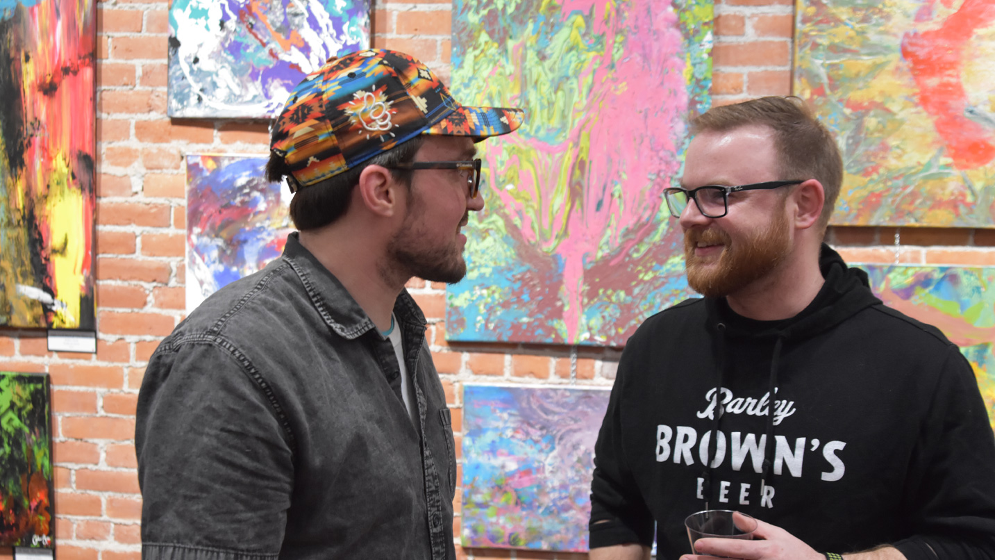 Two people talking in front of a wall of artwork.