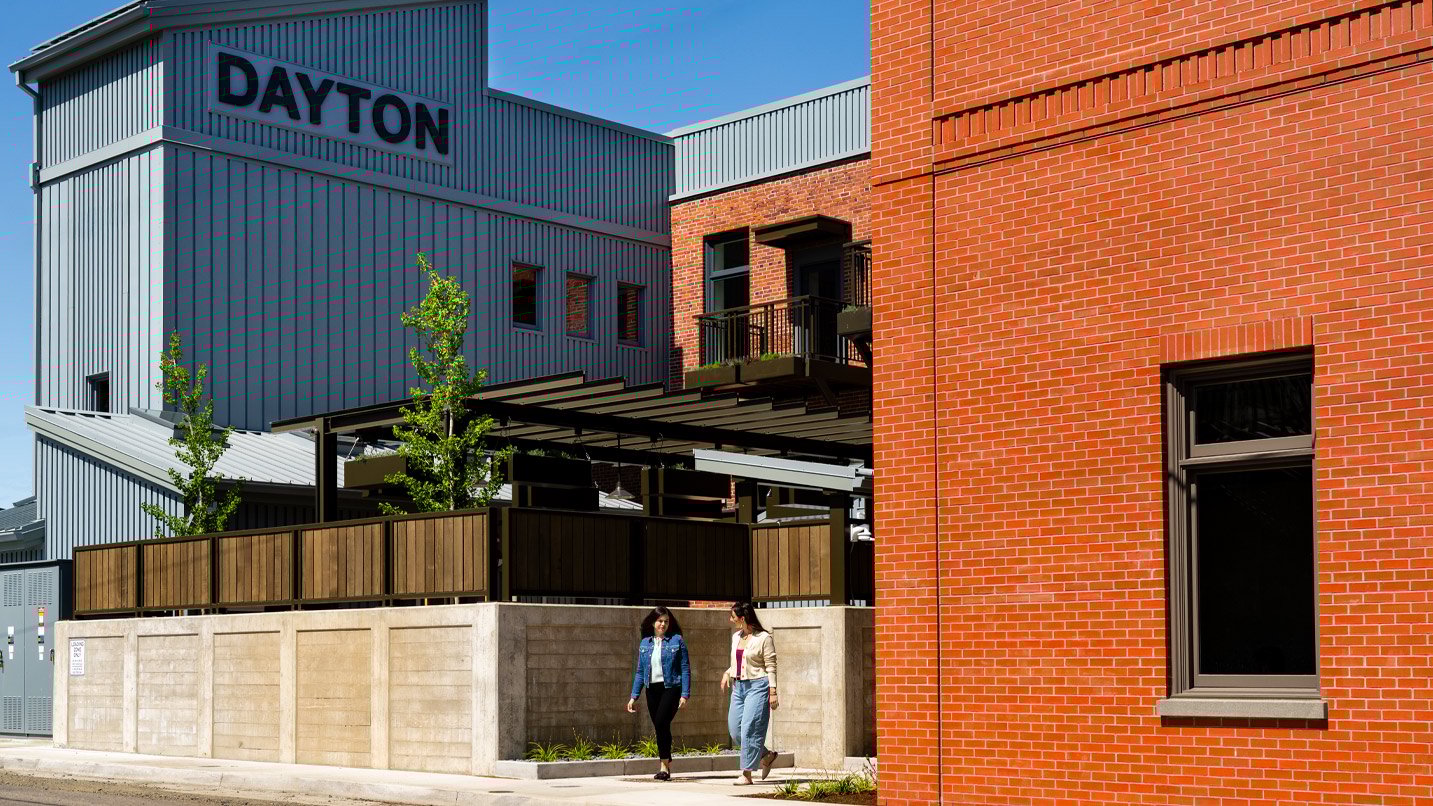 Two people walking out of a mix of modern and brick buildings.