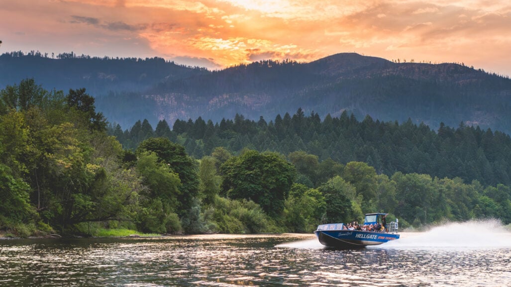 A jetboat glides down a river at sunset.