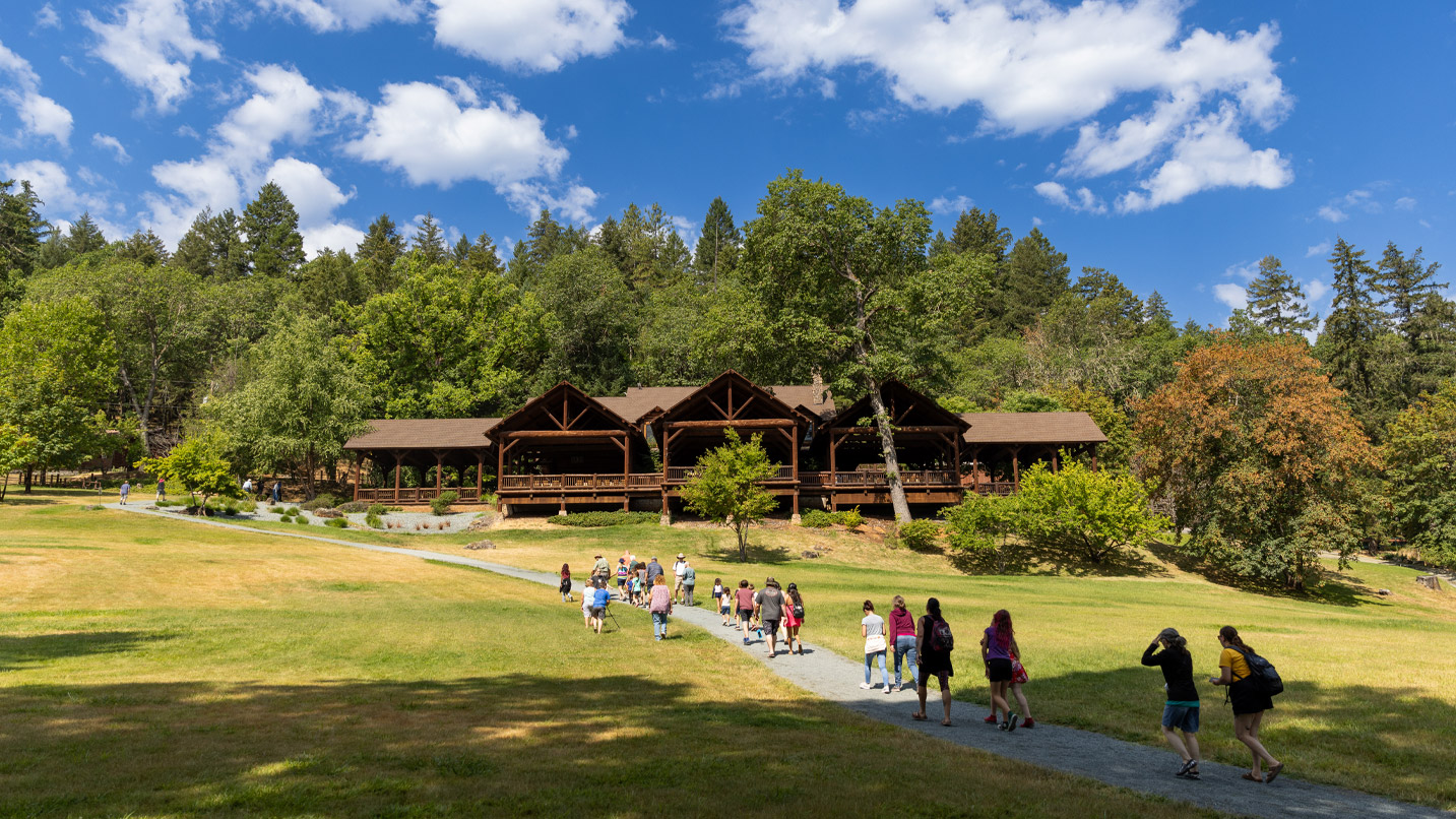A group of people walk up a hill to a log-cabin style building.