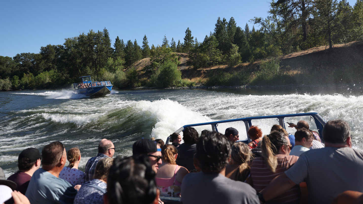 A jetboat full of people speeds through a river.