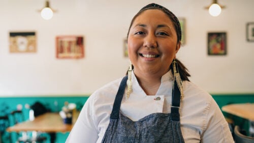 An indigenous woman stands inside a restaurant.