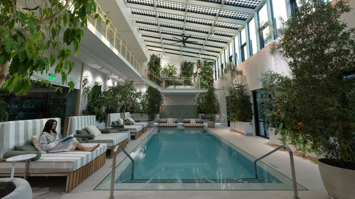 A large indoor pool area decorated with large plants and seating areas.