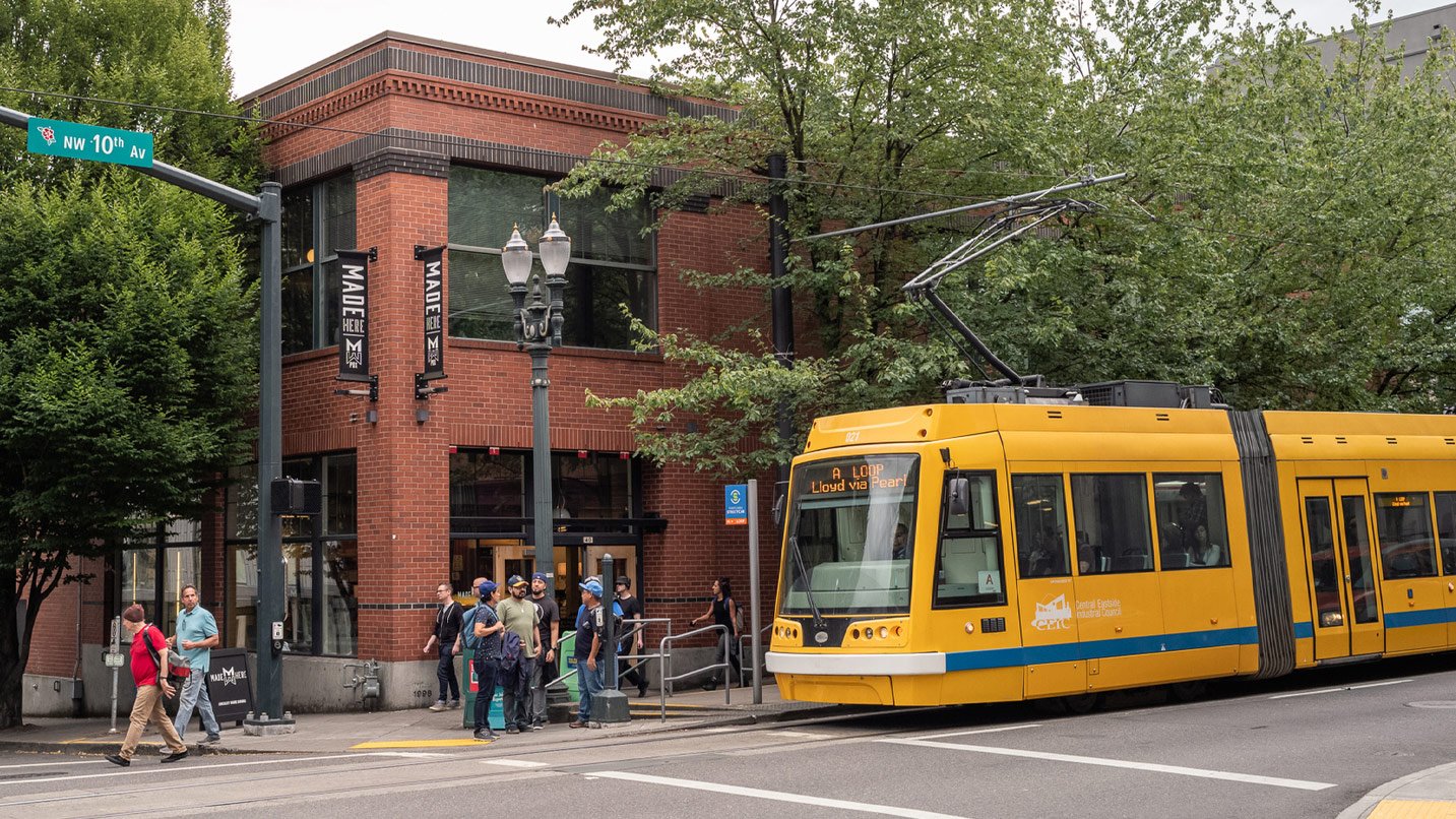 A yellow bus tram at a stop at a downtown Portland corner. People wait to cross the street.