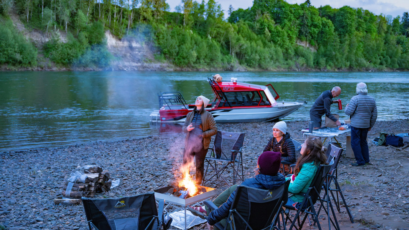 A group of people around a riverside campfire.
