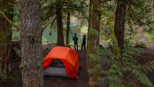 A red tent nestled in the woods above a river.