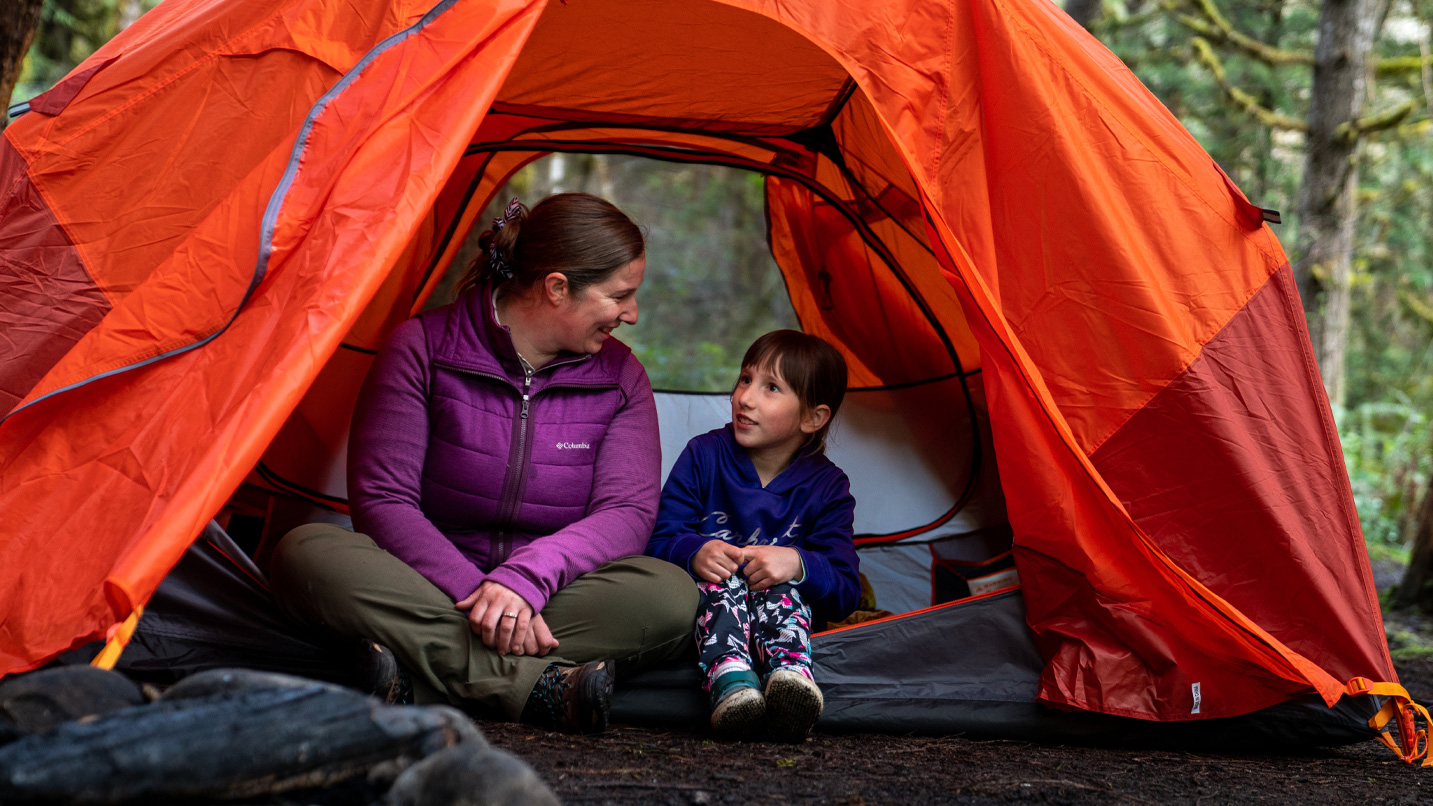 An adult and child sit in an unzipped tent.