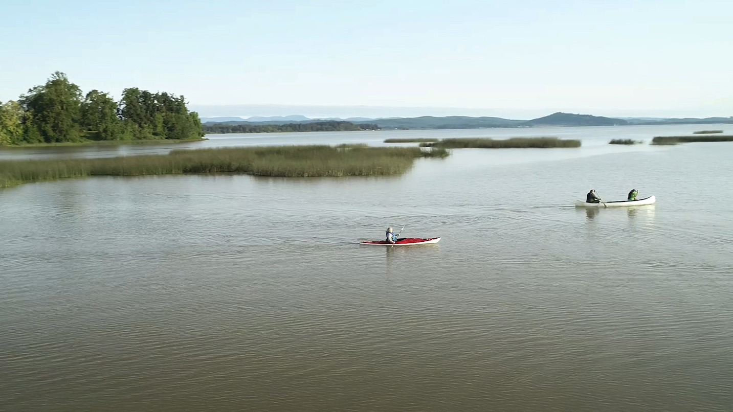 A kayaker and two people in a long canoe paddle along calm waters.