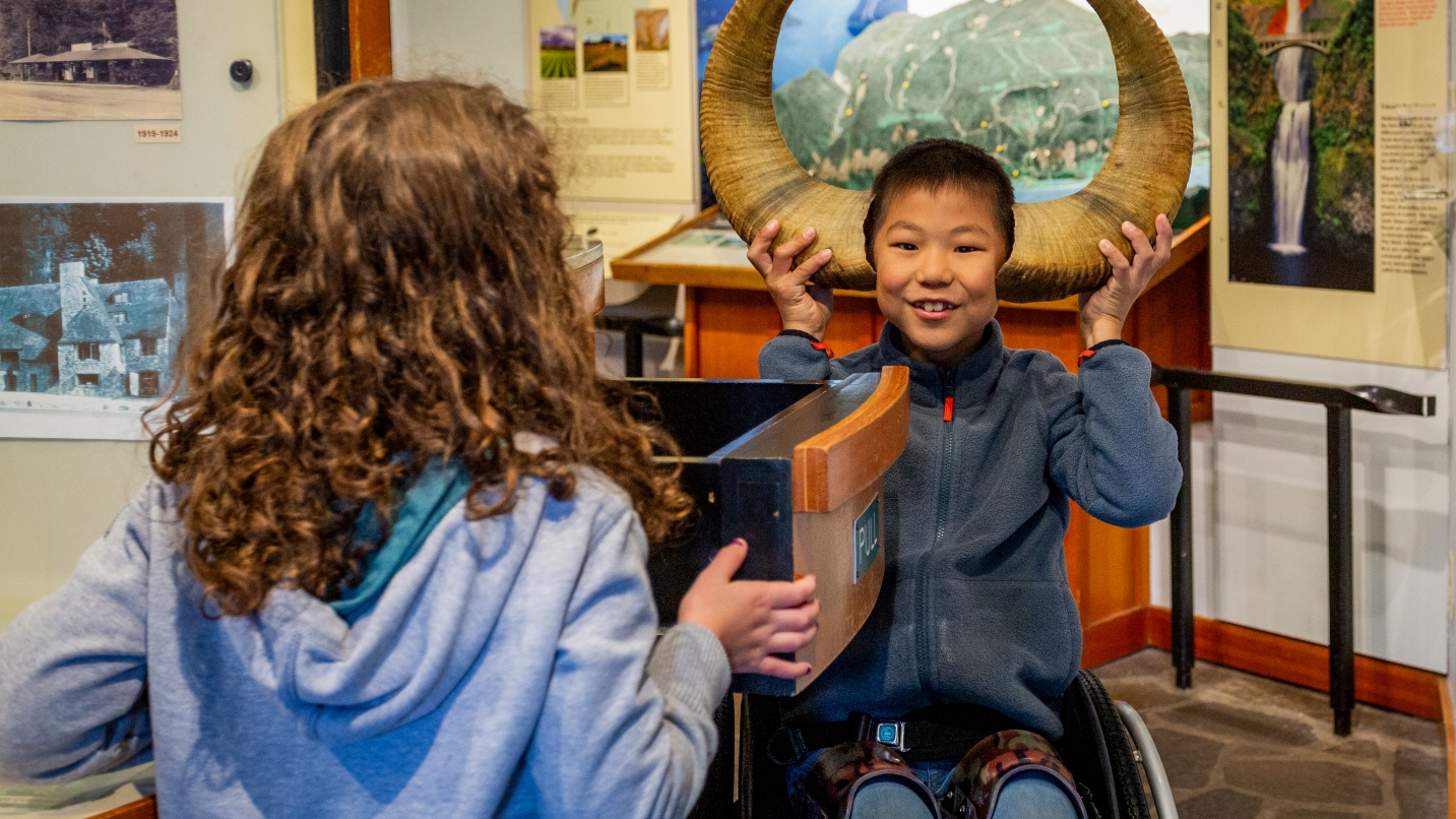 Boy holds big horns to side of head as girl watches