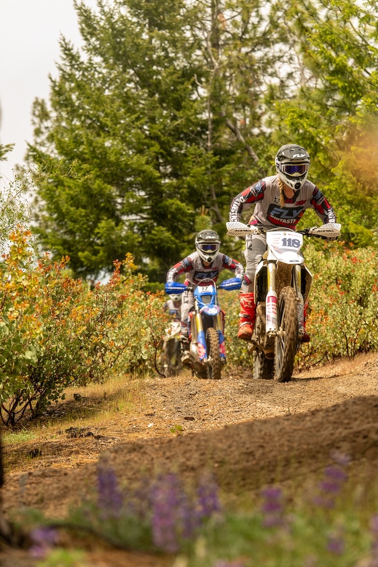 A line of dirt bikers travel along a dirt trail.