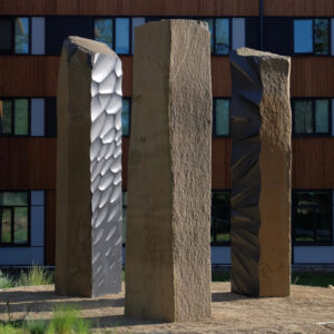 Three large monolithic columns placed outside of a building.