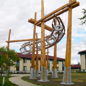 A hollow, rounded sculpture hangs from wooden pillars along a pathway.