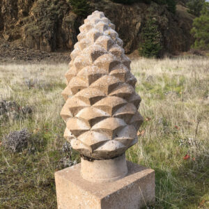 A sculpture of a pinecone sits on a pedestal in a field.