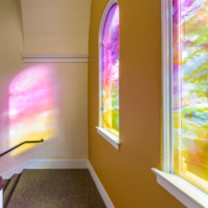 Light through brightly painted windows creates art on a wall.
