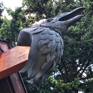 A sculpture of a bird attached to an outer-beam of a building.