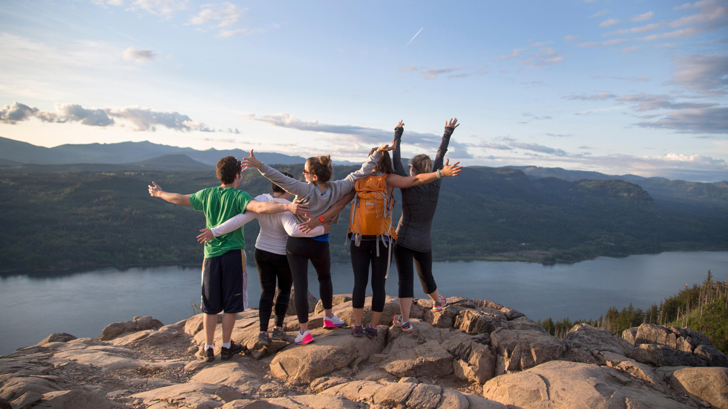 A group of people with their arms extended taking in the view of the Columbia River from a tall peak.