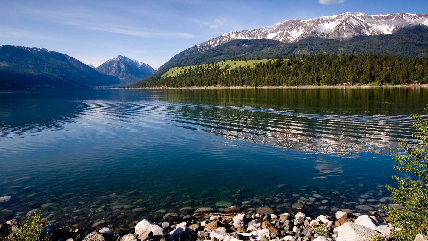 The rocky lakeshore of Wallowa Lake, surrounded by mountain range and tall conifers.
