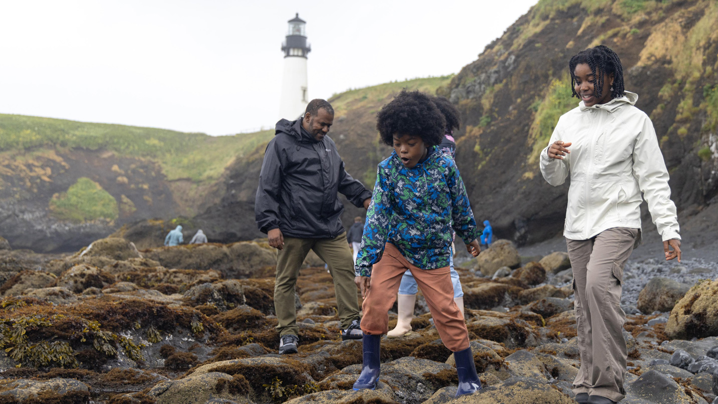 A family looks at tide pools below a light house.