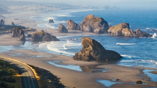 An aerial view of a road winding next to ocean sea stacks.