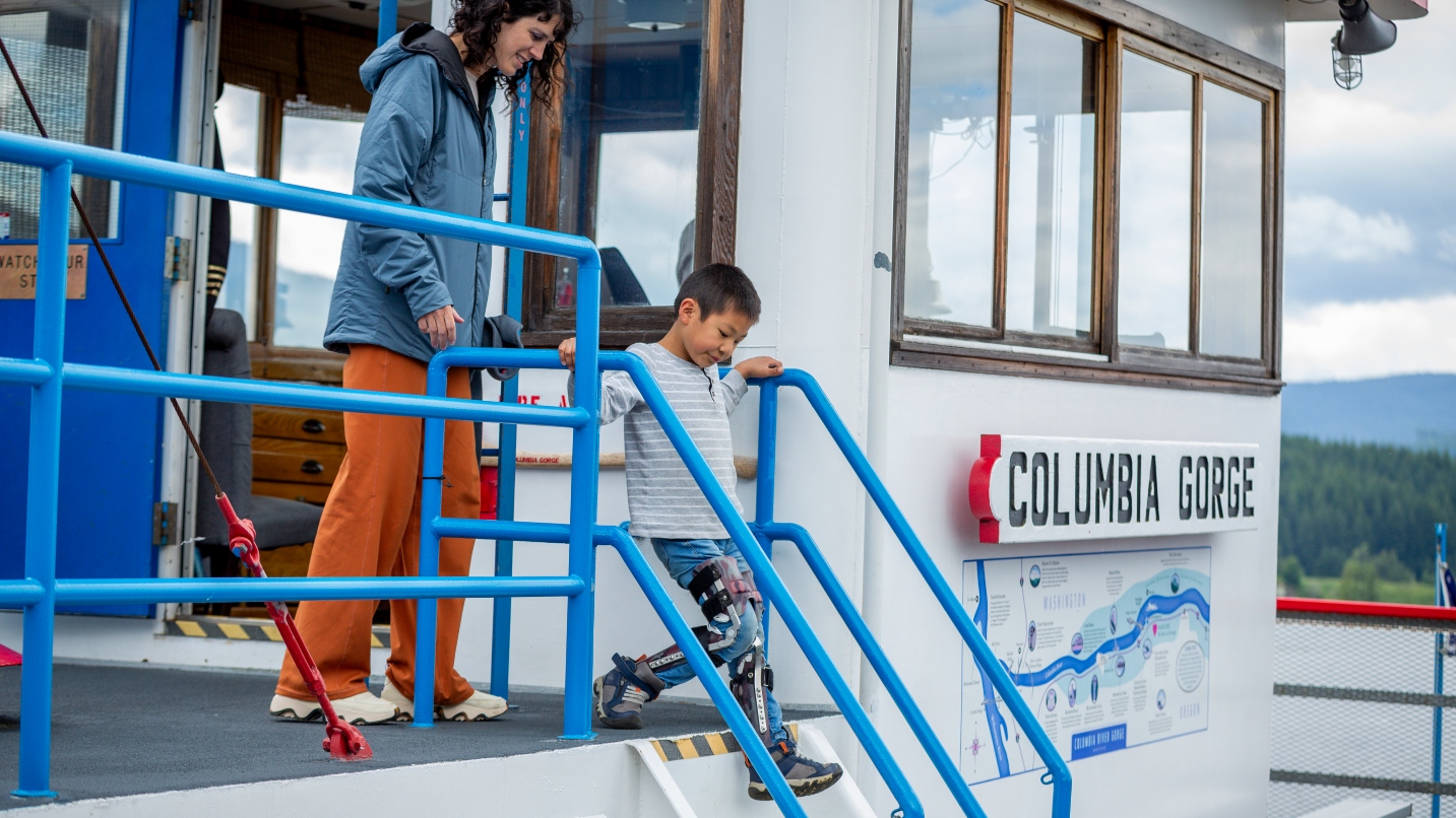 Woman watches as boy with leg braces steps down stairwell on a boat