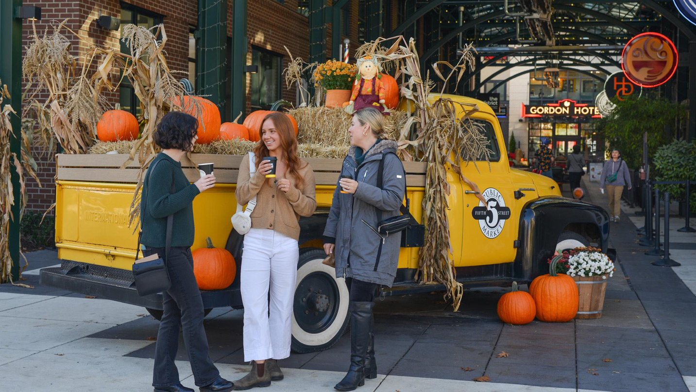 A classic truck filled with pumpkins is parked in a pedestrian walkway.