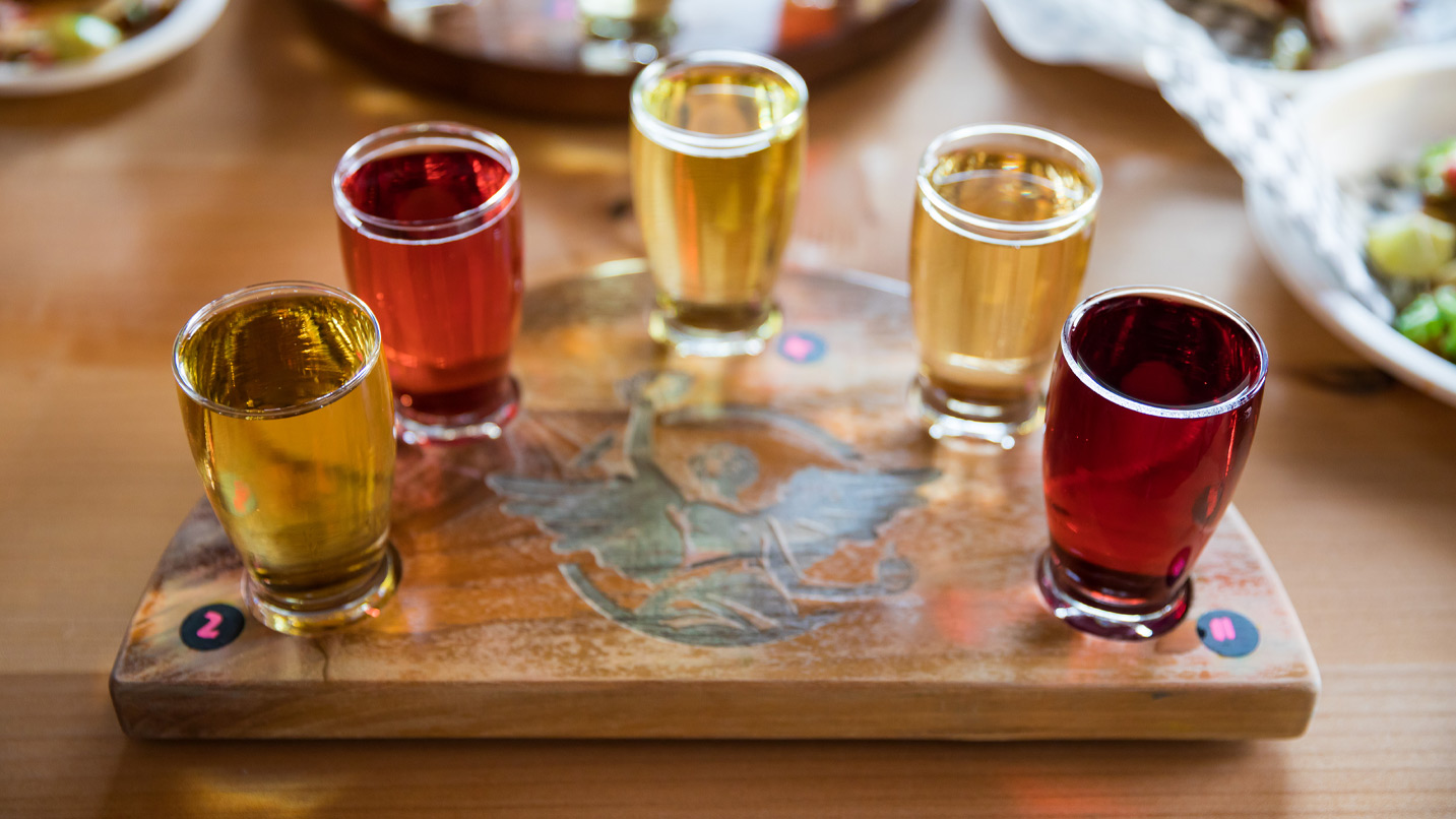 A flight of five ciders served on a wooden board.
