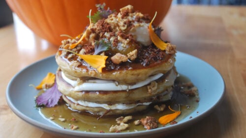 Stack of pancakes topped with syrup, nuts and edible petals.