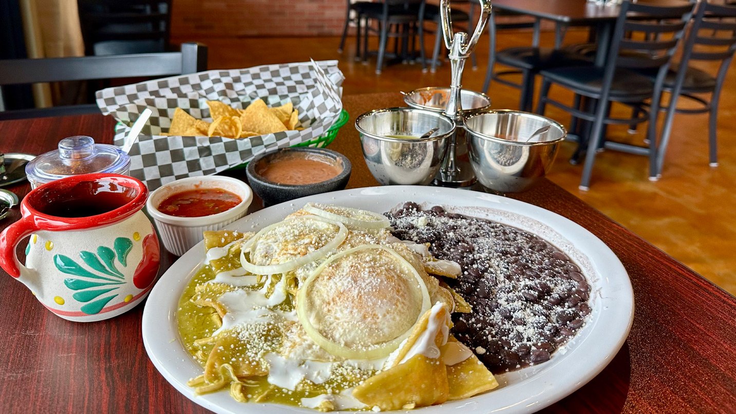 A plate of green chilaquiles and beans with a side of chips and salsa.