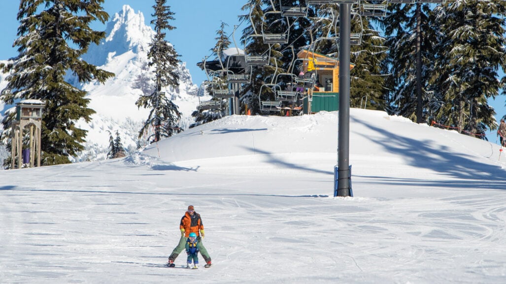 An adult skier guides a young child down a gentle slope.