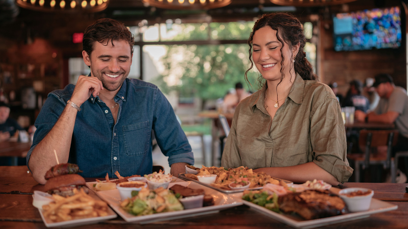 Two people sit at a bar with plates of food.