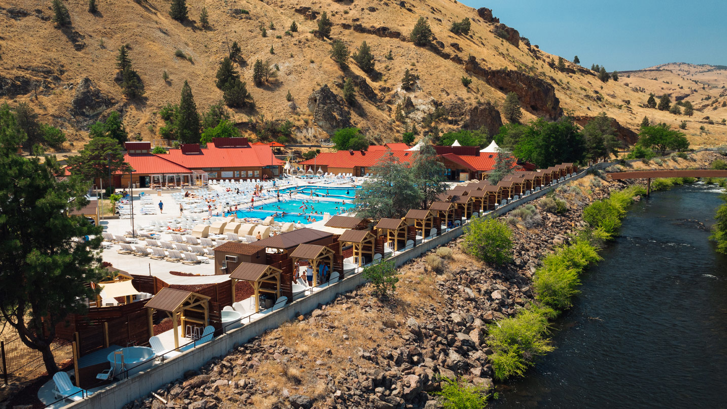 A lodge, pool and row of hot tubs sit above a riiver.
