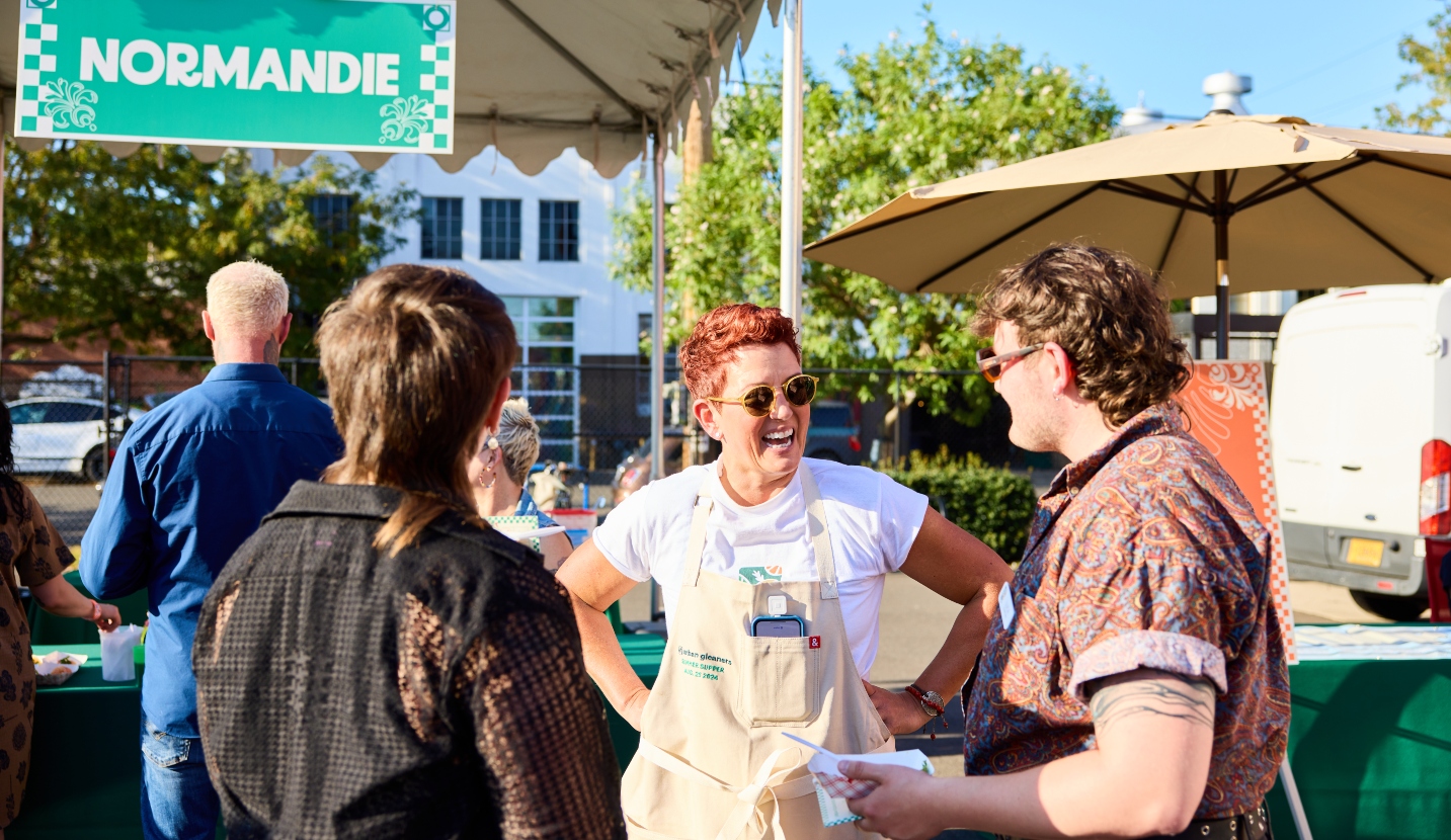 Three people talk in front of a tent serving food