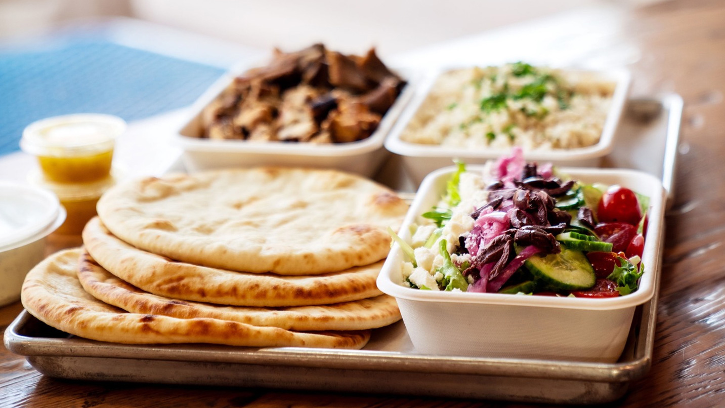 A tray with Mediterranean style foods, like cucumber salad and pita bread.