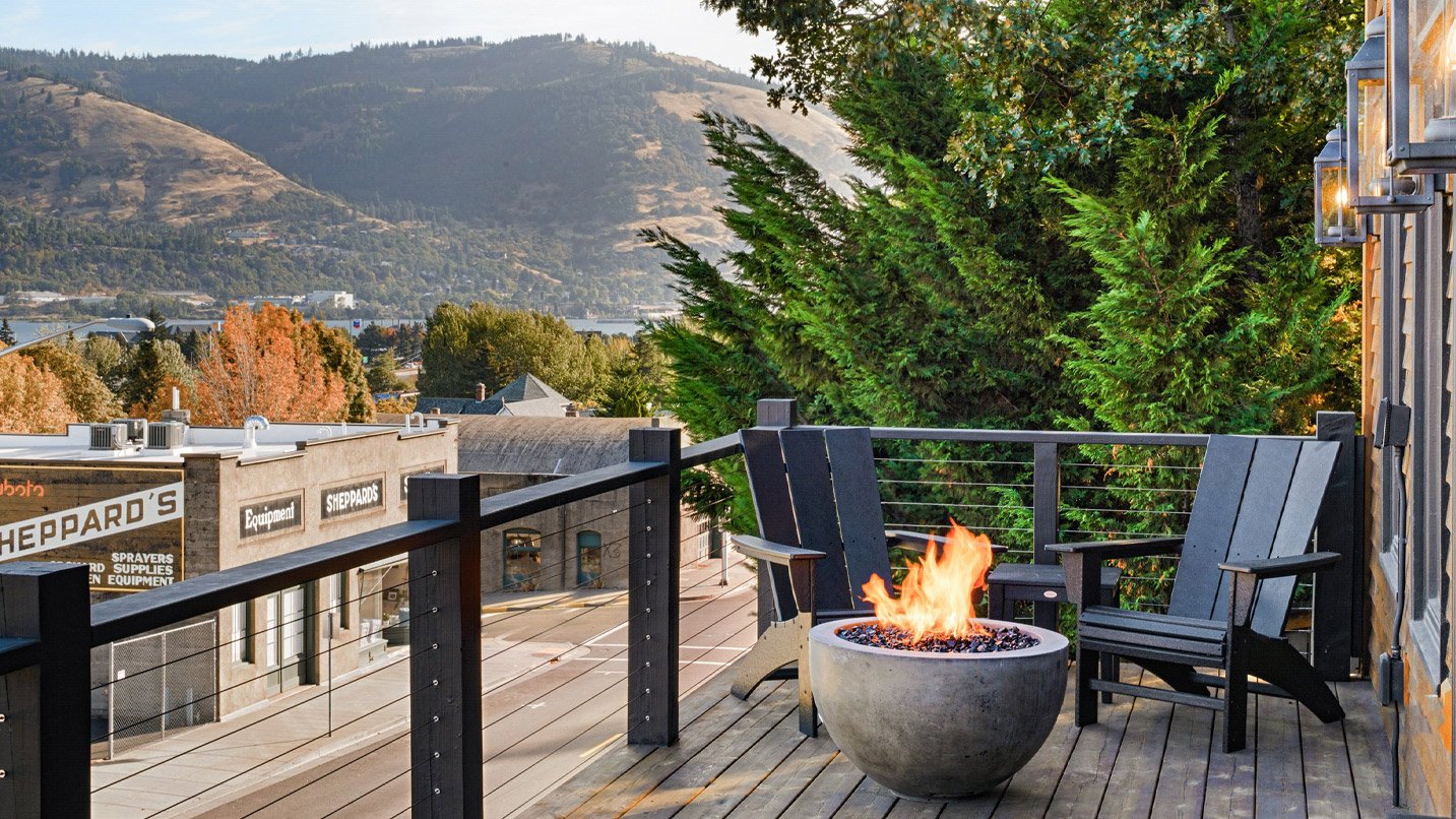 Balcony with a small firepit and chairs overlooking a a main road and mountains in the distance.