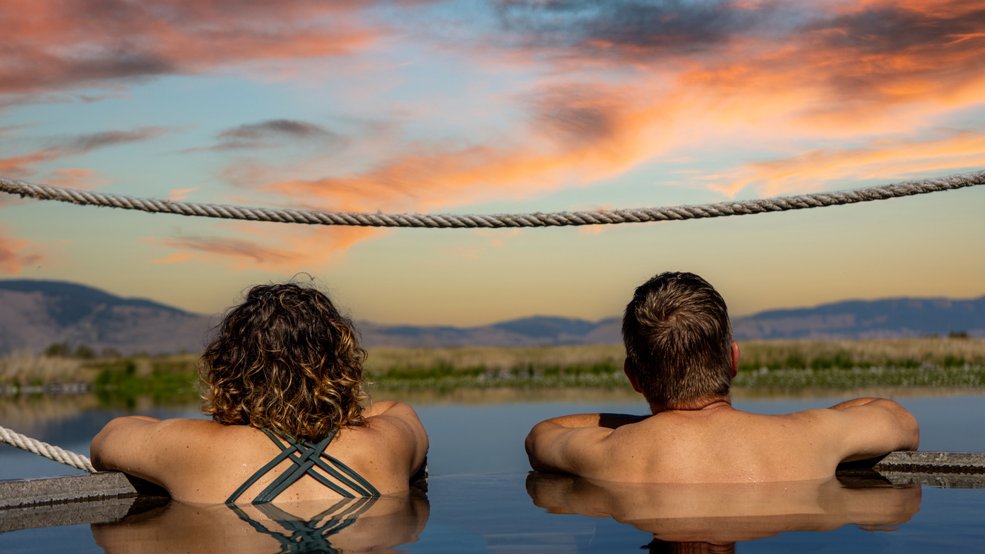 A man and a woman hang over the edge of a pool overlooking a natural spring.