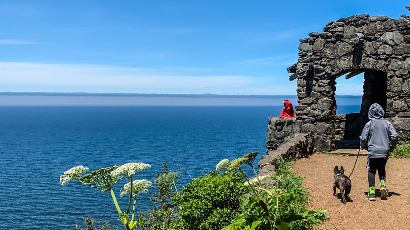 A boy with a dog walking up to a rustic stone building to a viewpoint.