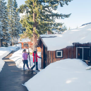 Two people walk into a snowy cabin holding their skis.