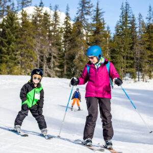 A child and adult ski down a mountain.