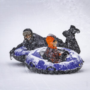 A father and young son tubing on a snowy day.