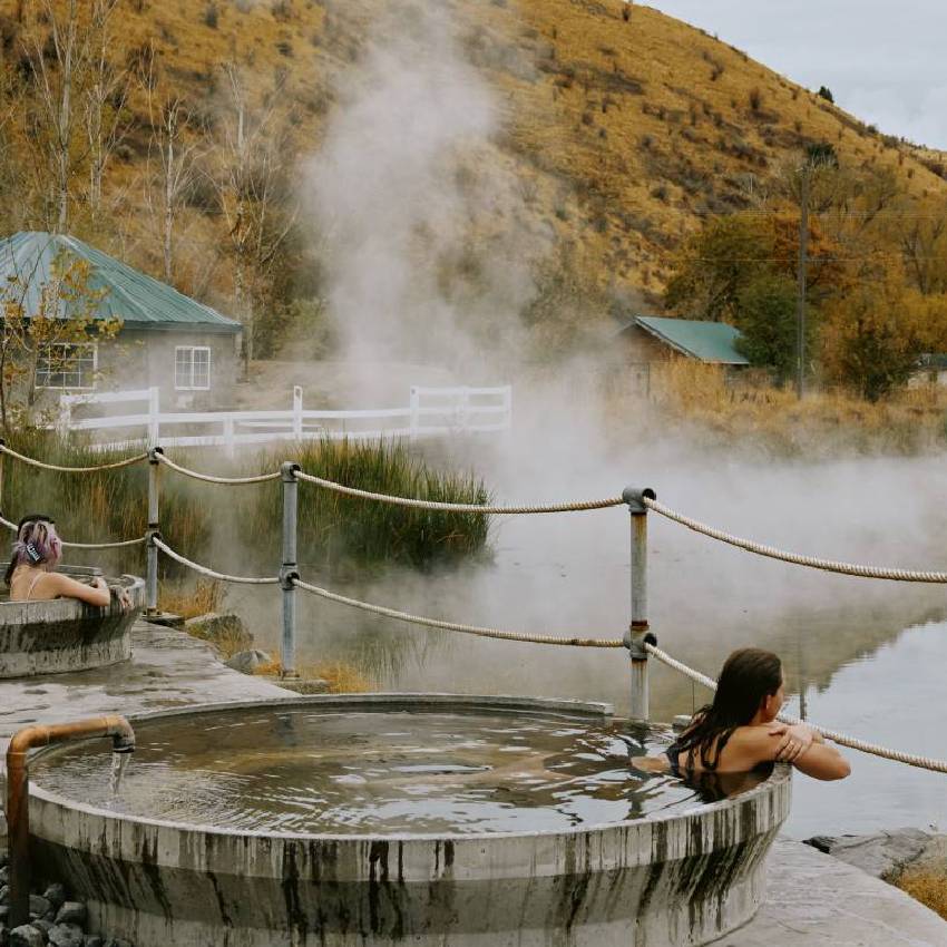 A woman in a concrete soaking pool overlooking a natural hot spring.