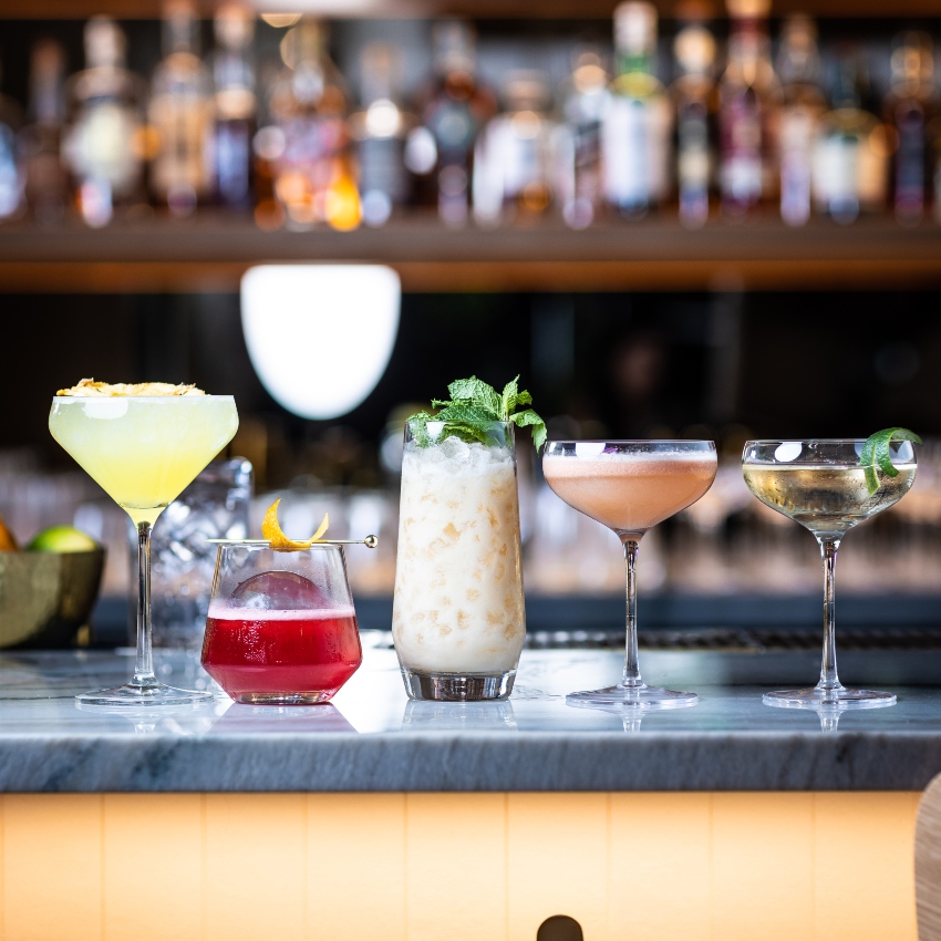 Different sized cocktails in a row on a sleek bar